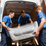 Removal team handling wrapped furniture beside a van